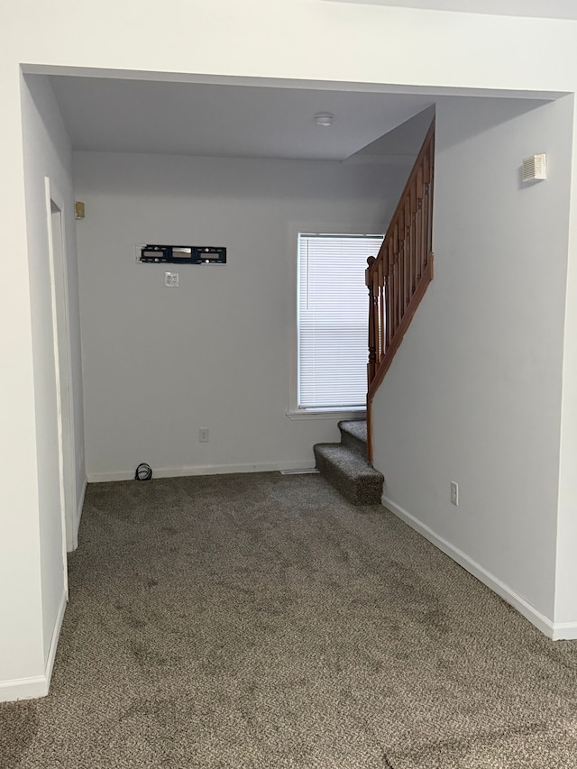 unfurnished room with stairs, baseboards, and dark colored carpet