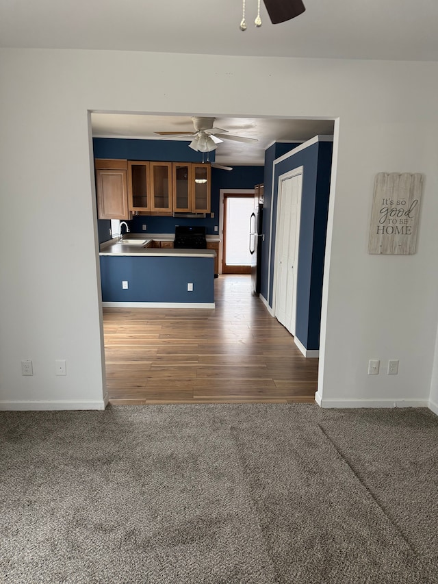 kitchen featuring brown cabinetry, glass insert cabinets, a peninsula, carpet flooring, and a sink