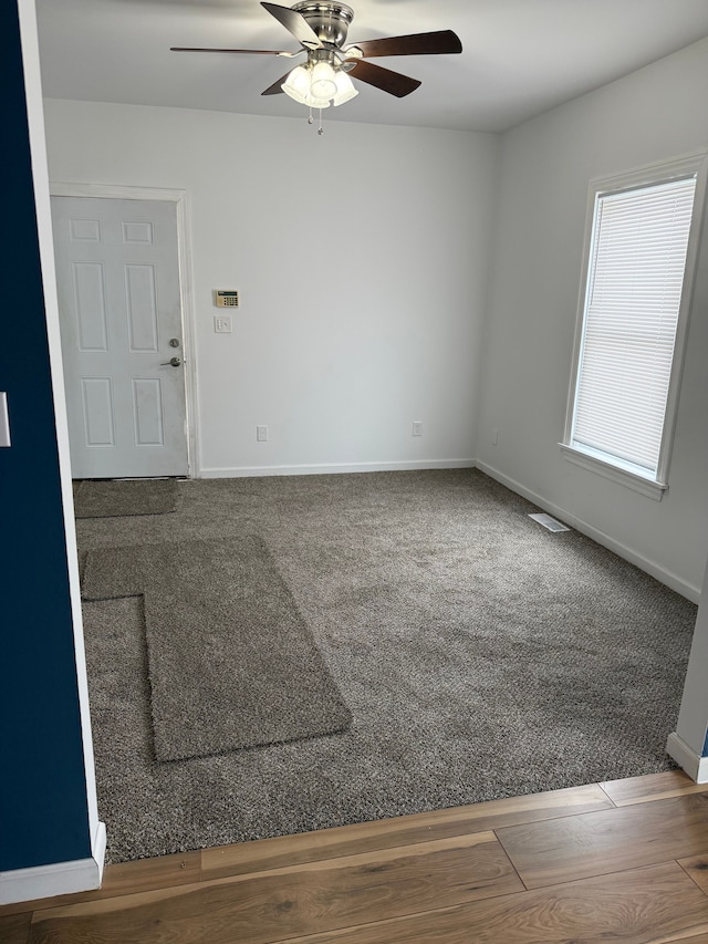 carpeted spare room with a ceiling fan, visible vents, baseboards, and wood finished floors