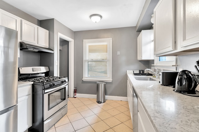 kitchen featuring white cabinets, appliances with stainless steel finishes, sink, light tile patterned flooring, and light stone counters