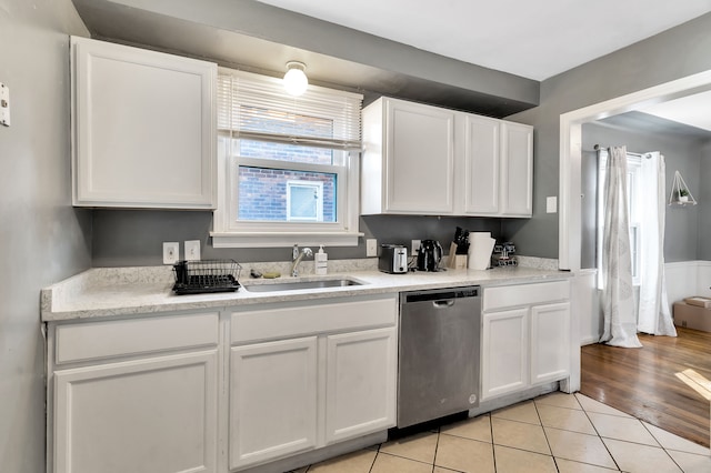 kitchen with sink, white cabinets, light tile patterned floors, and stainless steel dishwasher