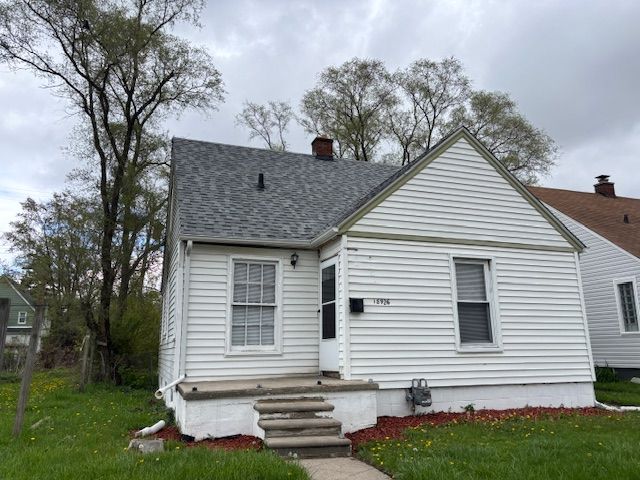 back of property with a chimney, a shingled roof, and a yard
