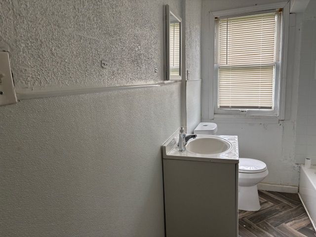 full bath featuring vanity, toilet, and a textured wall