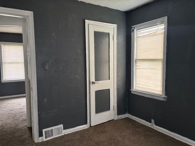 unfurnished bedroom featuring dark colored carpet, multiple windows, and baseboards