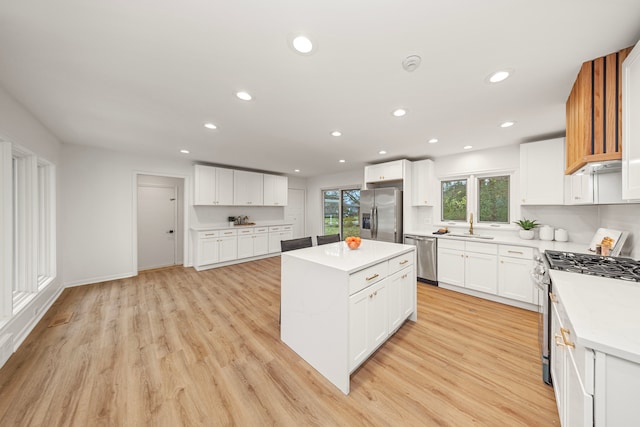 kitchen featuring appliances with stainless steel finishes, a center island, white cabinetry, light hardwood / wood-style floors, and sink