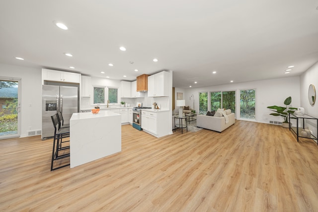 kitchen with white cabinets, a center island, light hardwood / wood-style floors, a breakfast bar area, and stainless steel appliances