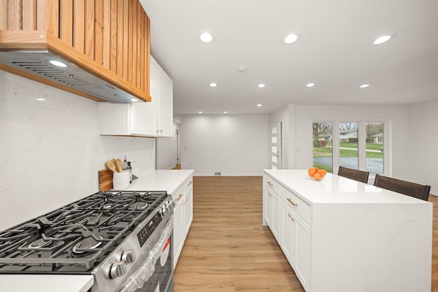 kitchen with a kitchen island, white cabinetry, light hardwood / wood-style floors, stainless steel range with gas cooktop, and custom range hood