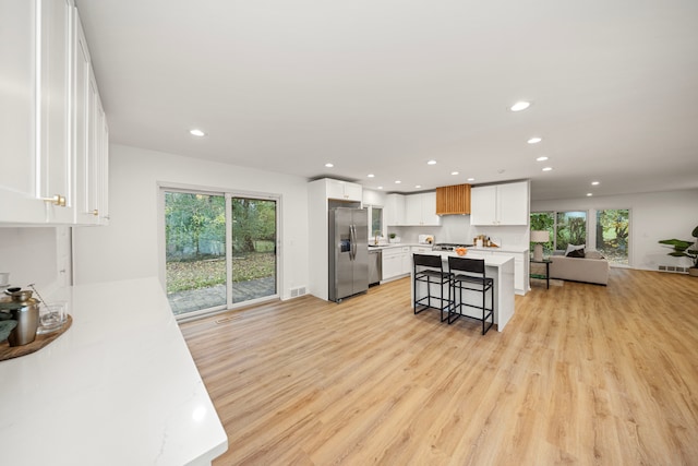 kitchen with light hardwood / wood-style flooring, white cabinets, a breakfast bar, a kitchen island, and stainless steel appliances