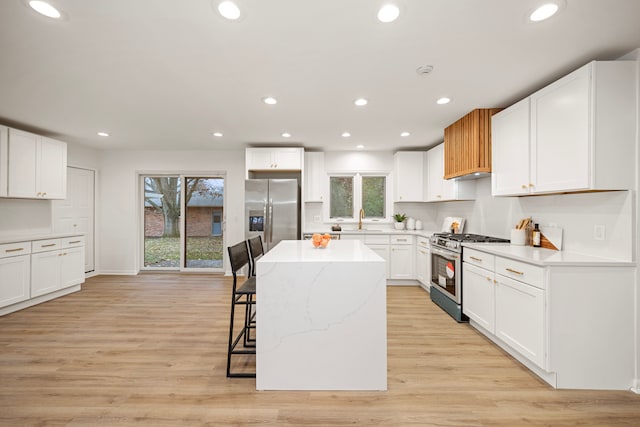 kitchen with a kitchen island, white cabinetry, stainless steel appliances, sink, and a breakfast bar area