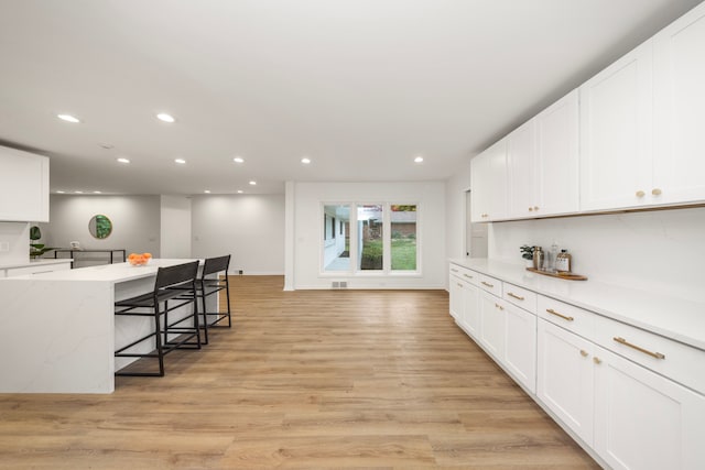 kitchen with white cabinets, a breakfast bar area, and light hardwood / wood-style floors