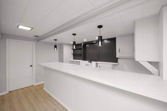 kitchen featuring white cabinets, decorative light fixtures, kitchen peninsula, and light wood-type flooring