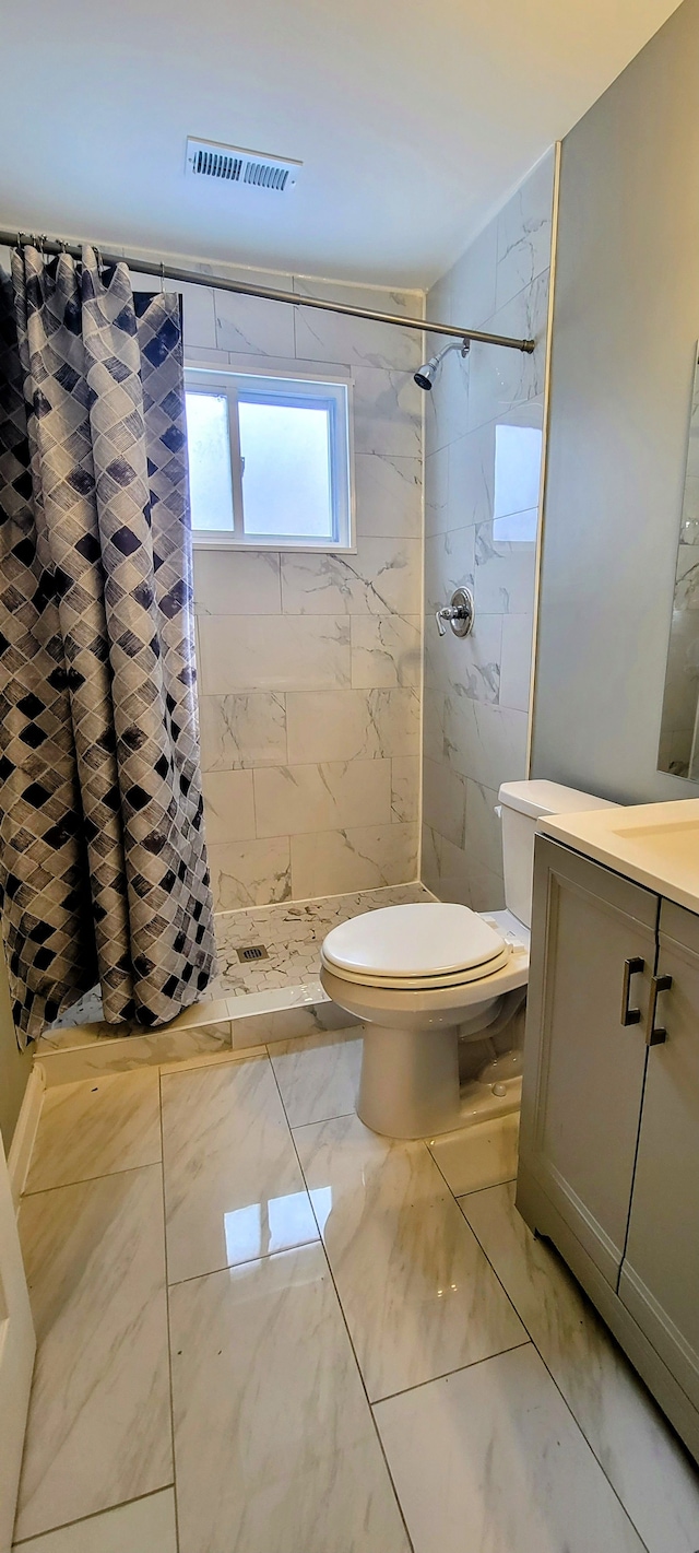 bathroom featuring visible vents, toilet, a tile shower, marble finish floor, and vanity