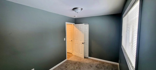 spare room with baseboards and light colored carpet