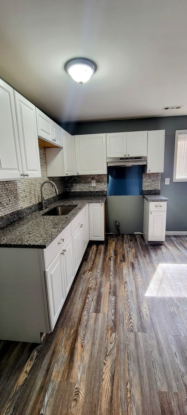 kitchen featuring a sink, dark wood-style floors, white cabinetry, dark stone counters, and decorative backsplash