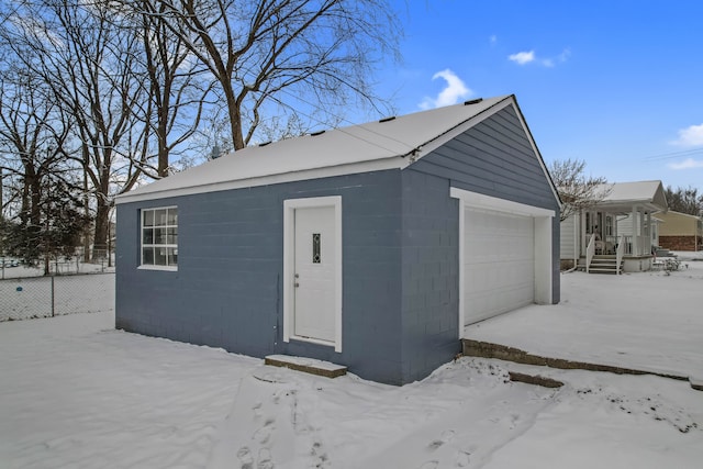 snow covered garage with a detached garage and fence