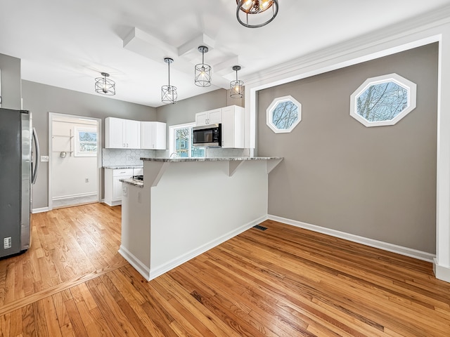 kitchen with light stone counters, a peninsula, stainless steel appliances, white cabinetry, and backsplash