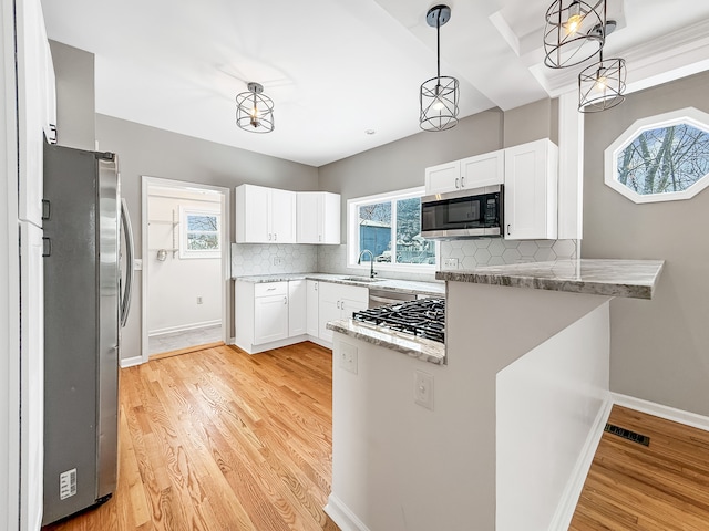 kitchen with appliances with stainless steel finishes, a peninsula, light wood finished floors, and tasteful backsplash