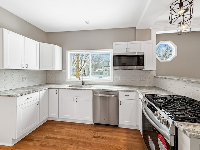 kitchen with stainless steel appliances, light wood finished floors, a sink, and light stone countertops