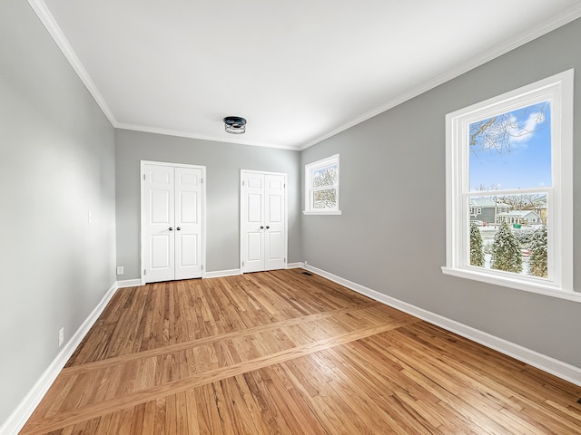 unfurnished bedroom featuring ornamental molding, light wood-style flooring, baseboards, and two closets