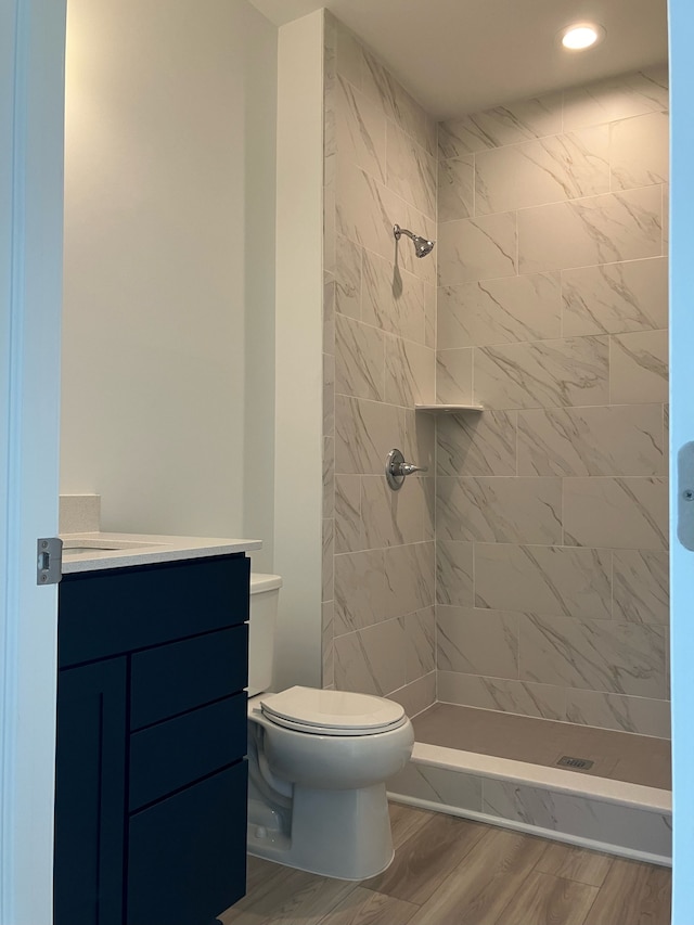 bathroom with hardwood / wood-style flooring, toilet, tiled shower, and vanity