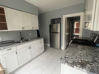 kitchen featuring sink, white cabinetry, light stone counters, range, and stainless steel fridge