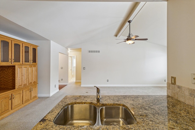 kitchen with ceiling fan, sink, light colored carpet, lofted ceiling with beams, and dark stone counters