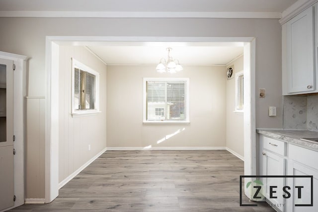 unfurnished dining area featuring crown molding, plenty of natural light, a notable chandelier, and light hardwood / wood-style floors