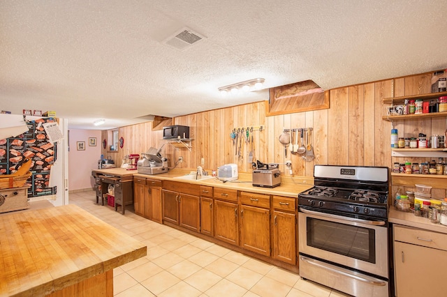 kitchen featuring stainless steel gas stove, sink, light tile patterned floors, a textured ceiling, and wooden walls