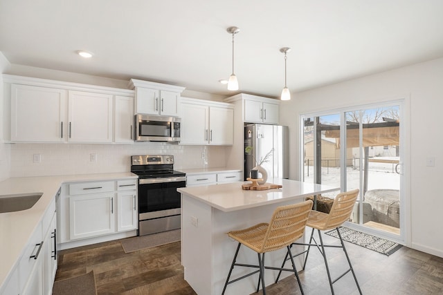 kitchen with a kitchen island, white cabinets, hanging light fixtures, and appliances with stainless steel finishes