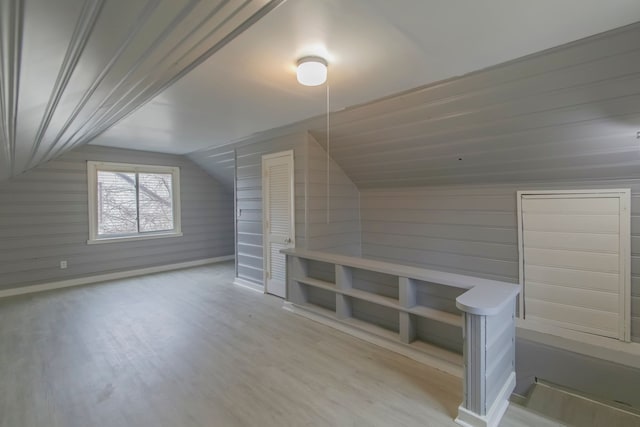 bonus room featuring light hardwood / wood-style floors, wooden walls, and vaulted ceiling