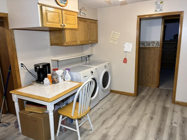 clothes washing area featuring light wood-type flooring, washing machine and dryer, baseboards, and a textured ceiling