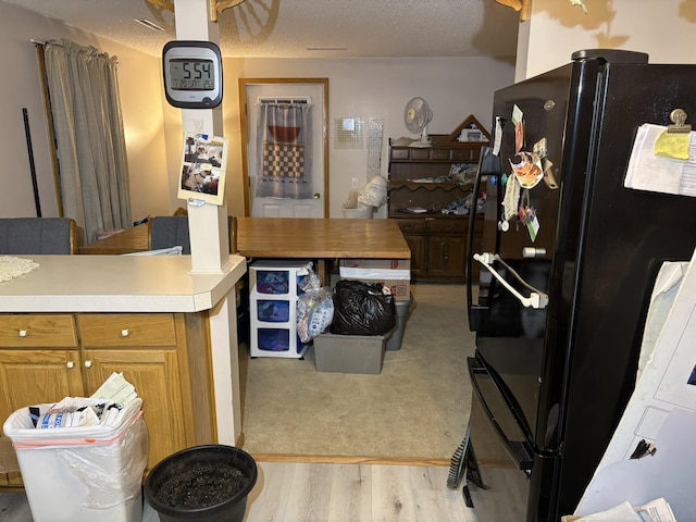 kitchen featuring a textured ceiling, light wood-type flooring, and black fridge