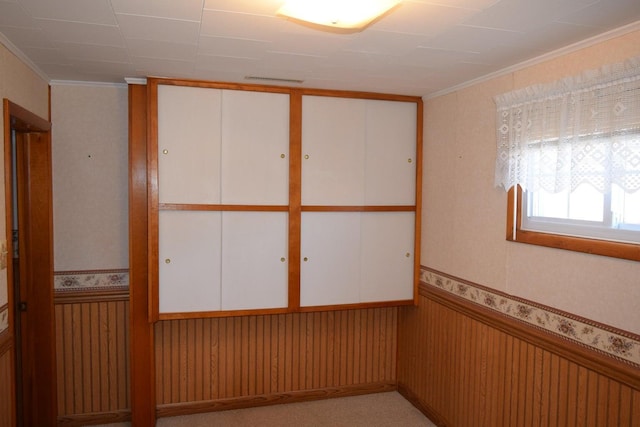 unfurnished room featuring light carpet, a wainscoted wall, and crown molding