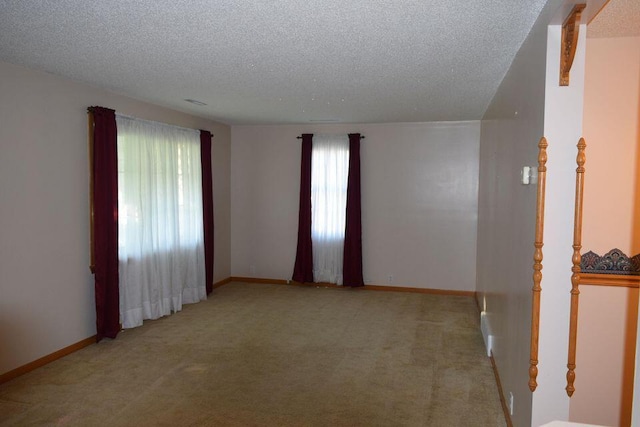 empty room featuring light carpet, baseboards, and a textured ceiling