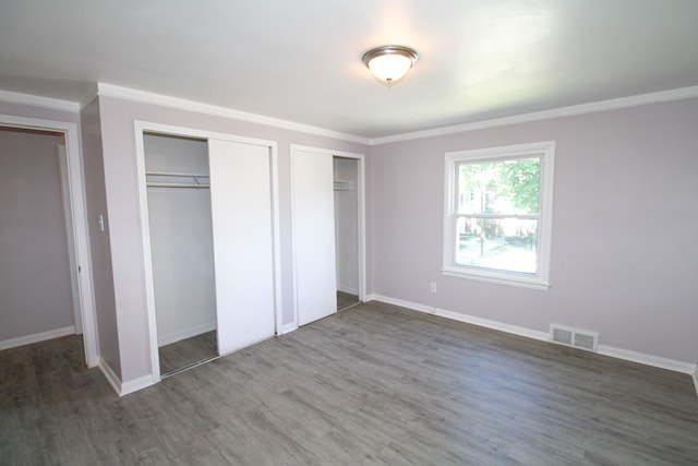 unfurnished bedroom featuring dark wood-type flooring, ornamental molding, and multiple closets