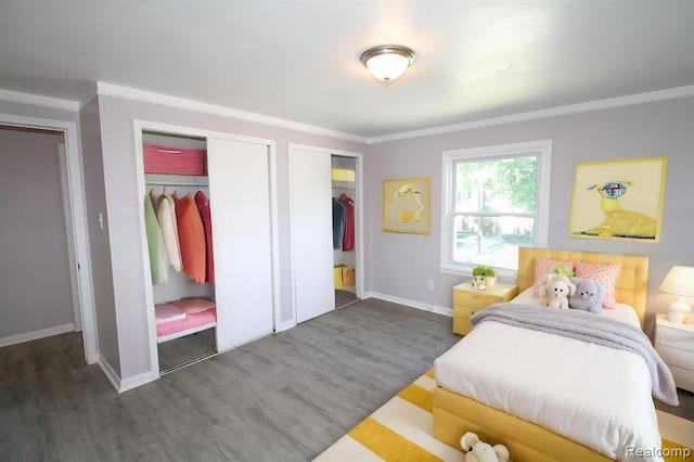 bedroom with two closets, dark hardwood / wood-style floors, and ornamental molding