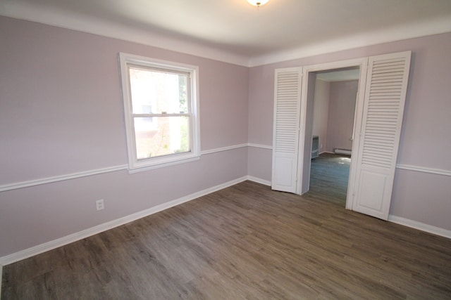 unfurnished bedroom featuring baseboard heating, dark wood-type flooring, and a closet