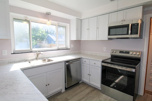 kitchen with white cabinets, stainless steel appliances, sink, and decorative light fixtures