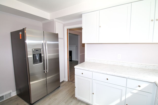 kitchen featuring light stone countertops, white cabinets, light hardwood / wood-style floors, stainless steel fridge with ice dispenser, and crown molding