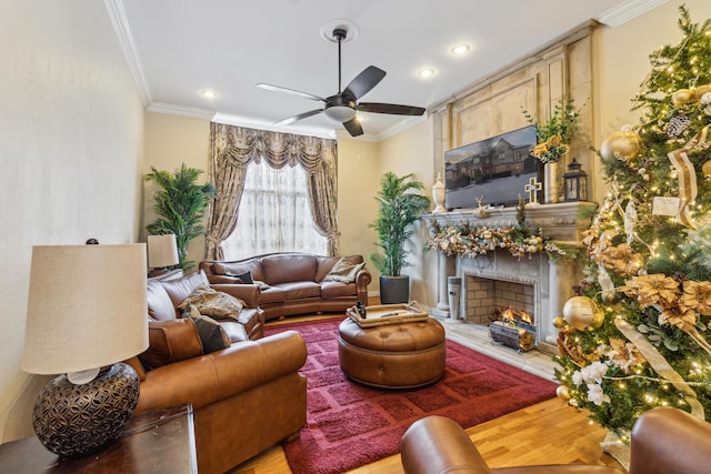 living room with ceiling fan, a tile fireplace, ornamental molding, and light wood-type flooring