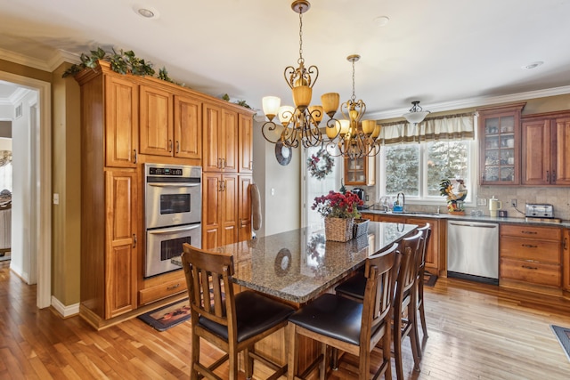 kitchen featuring a kitchen breakfast bar, pendant lighting, appliances with stainless steel finishes, light wood-type flooring, and dark stone countertops