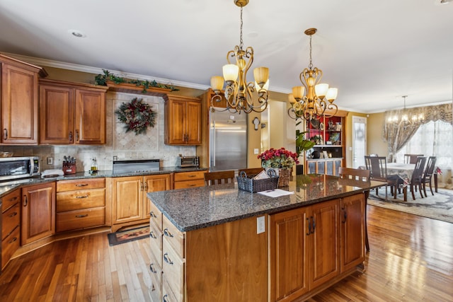 kitchen with light hardwood / wood-style floors, a chandelier, hanging light fixtures, a kitchen island, and backsplash