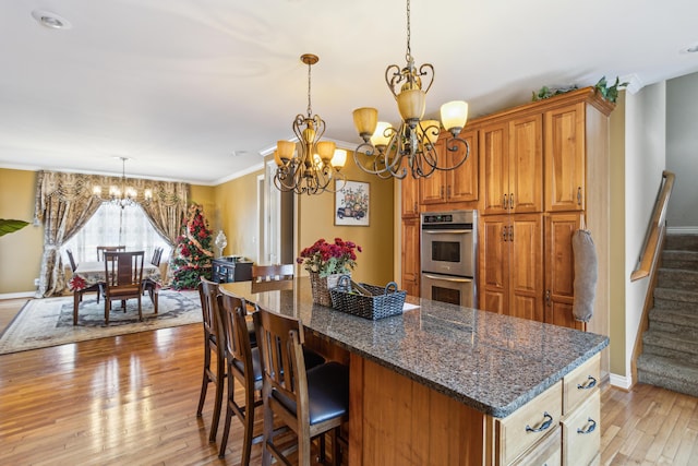 kitchen with double oven, light wood-type flooring, dark stone countertops, a chandelier, and a breakfast bar area