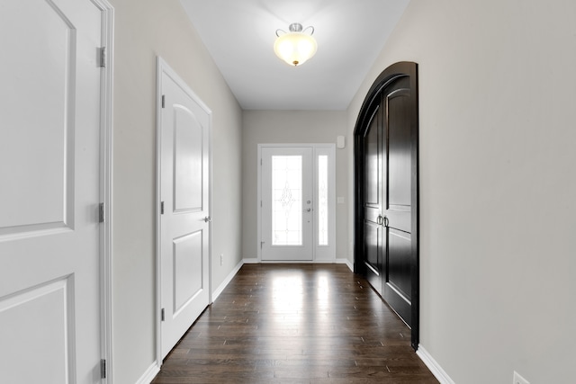 doorway with baseboards, arched walkways, and dark wood-type flooring