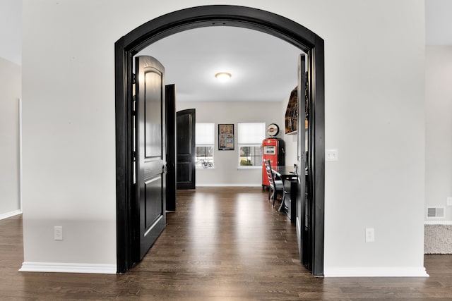 hall featuring arched walkways, visible vents, baseboards, and wood finished floors