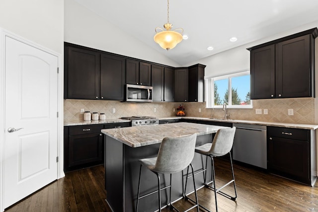 kitchen featuring dark wood finished floors, a center island, light stone countertops, vaulted ceiling, and stainless steel appliances