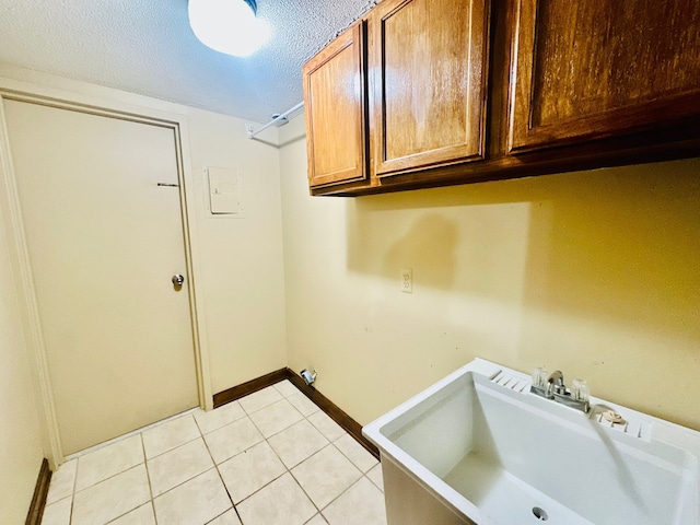 laundry area featuring sink, a textured ceiling, light tile patterned floors, and cabinets