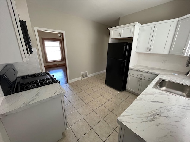 kitchen with white cabinets, decorative backsplash, black fridge, and gas range