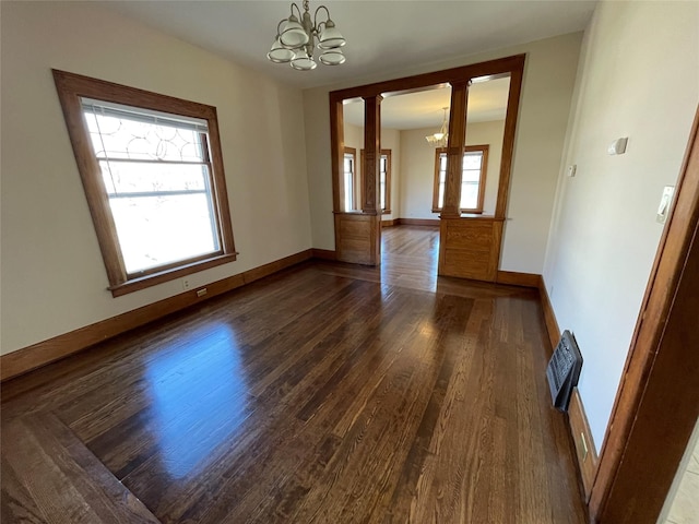 empty room with a chandelier, dark hardwood / wood-style floors, and ornate columns