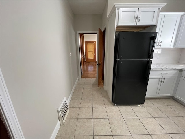 kitchen featuring light stone countertops, tasteful backsplash, white cabinetry, black fridge, and light tile patterned flooring